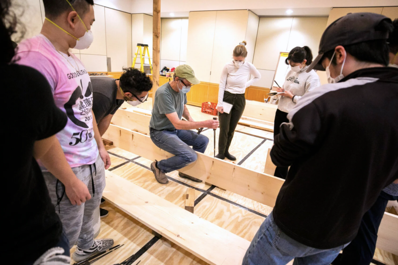 学生们聚集在道格拉斯·布鲁克斯教练周围，他们正在建造一艘日本内河小艇