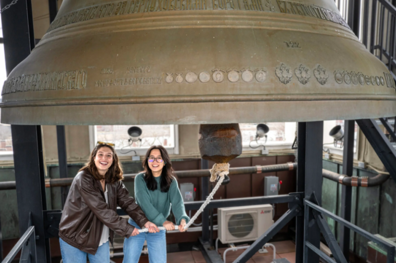 Sofia Giannuzzi (left) and Linh Vu ring a large bell in the Lowell House bell tower as part of a Sunday House tradition.