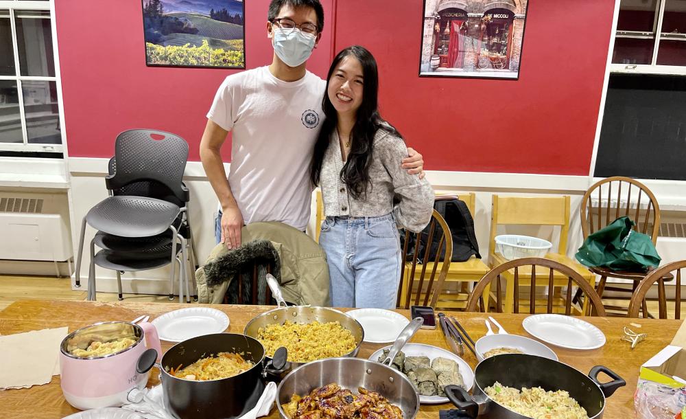Janny and Raymond standing in front of a table covered in plates and pots with food.