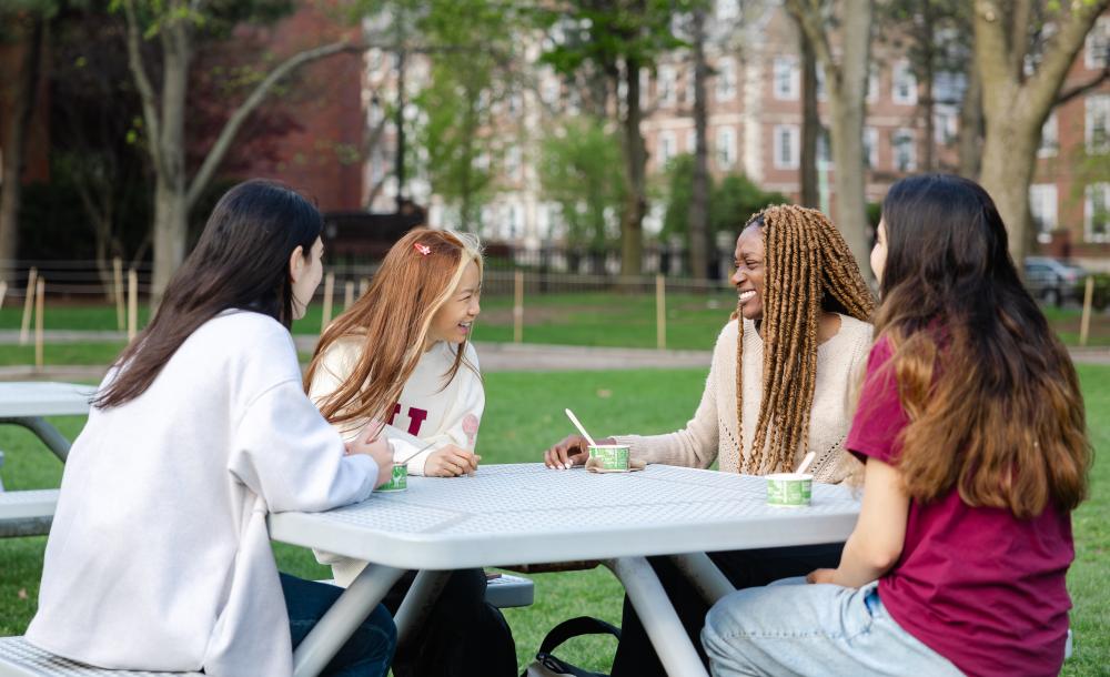 4 femal students laughing and eating ice cream at a table in JFK park