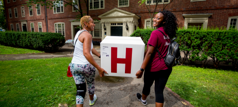 A student and her mother carry a box into a dorm for first-year move-in day