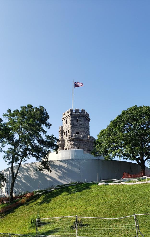 tower with flag flying, on a grassy hill with trees