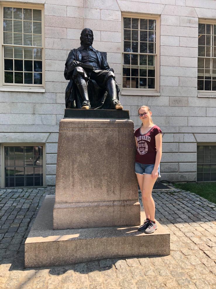 A photo of a female standing in front of the John Harvard statue,
