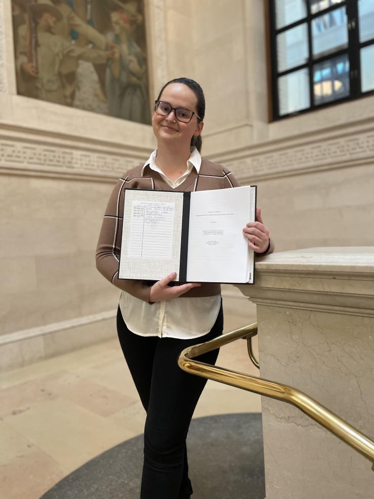 Photo of a female holding her senior thesis in Harvard's Widener Library
