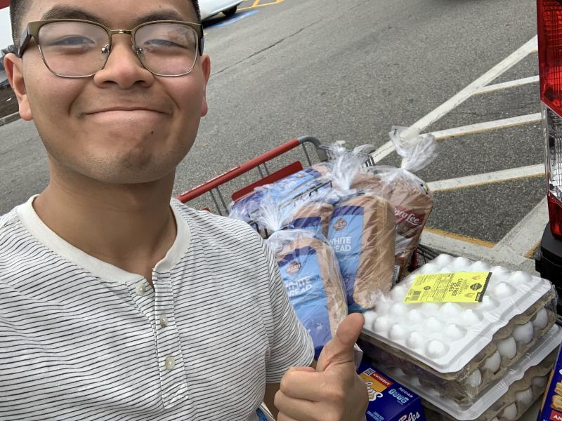 Selfie-style image of a person smiling in front of a shopping cart full of food items.