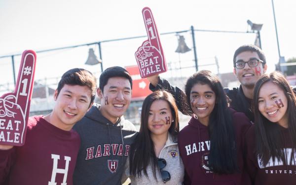 Six Harvard students with foam fingers cheering for Harvard-Yale football game