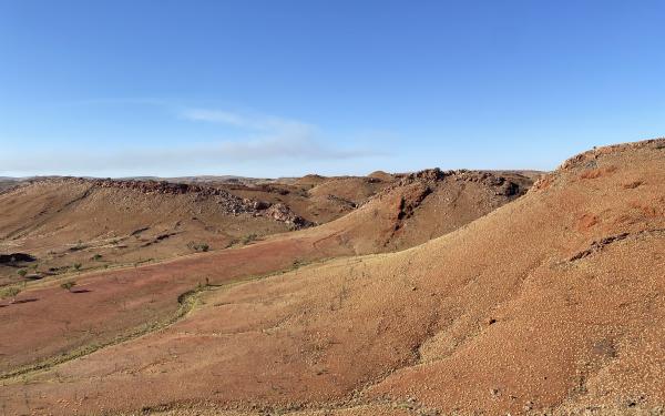 View of the Pilbara, showing sprawling hills dotted with pale green spinifex bushes on vibrant red dirt. 