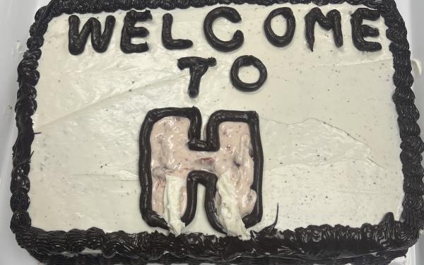 Image of a cake with white and black frosting and the words “Welcome to H” written on top.