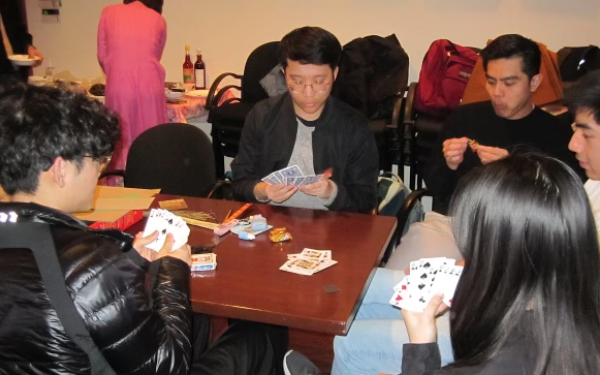 A group of five people playing cards at a table.