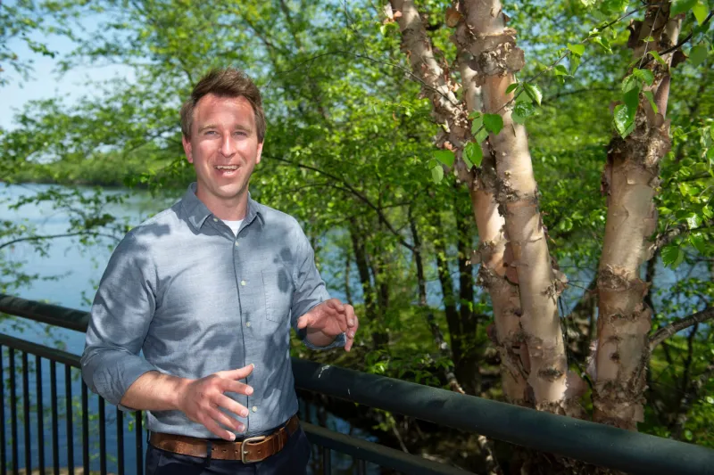 Jeffrey Wilson smiles next to a tree and in front of a water body