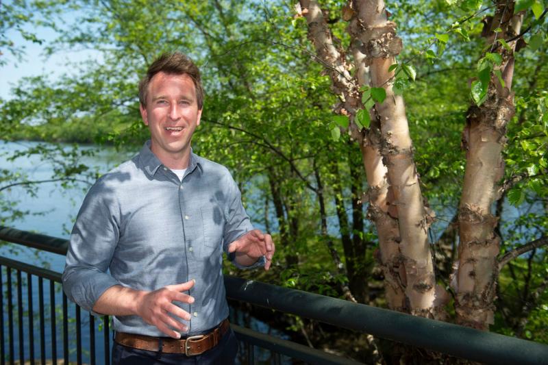 Jeffrey Wilson smiles next to a tree and in front of a water body