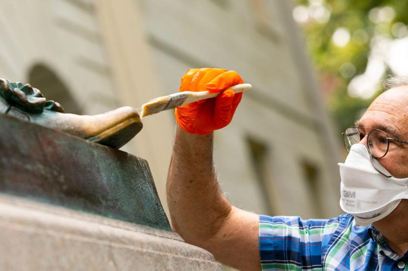 John Harvard's statue's foot being brushed during the renovation process