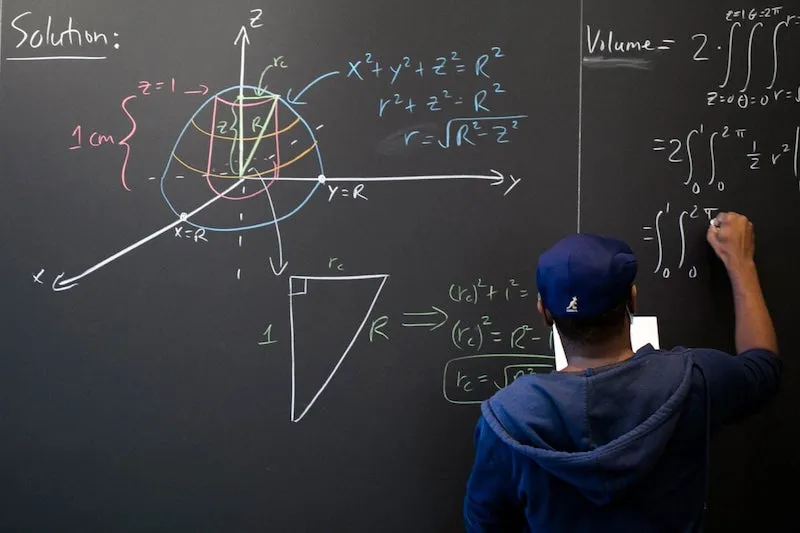 Hakim Walker, preceptor of mathematics, uses the chalkboard in the Science Center math lounge to try to solve a problem: finding the volume of a ball with a 2-centimeter-long cylindrical hole drilled through it.