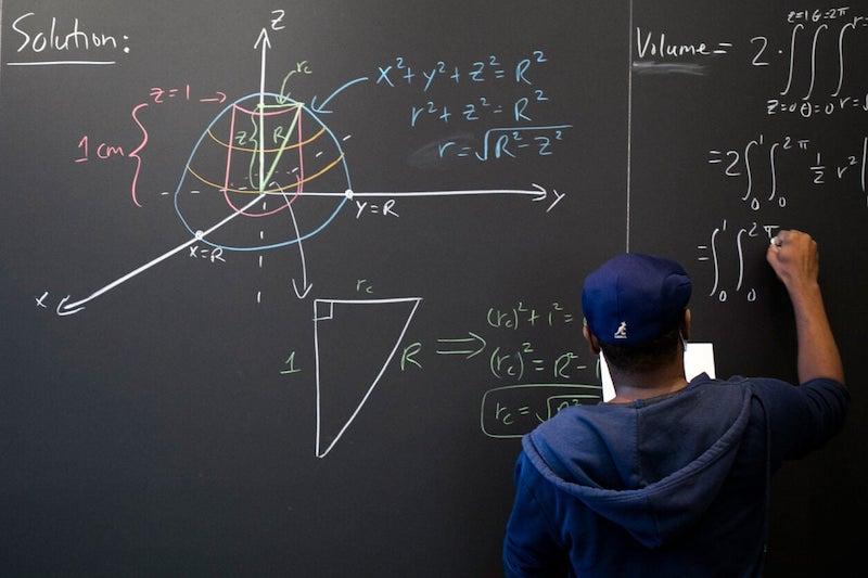 Hakim Walker, preceptor of mathematics, uses the chalkboard in the Science Center math lounge to try to solve a problem: finding the volume of a ball with a 2-centimeter-long cylindrical hole drilled through it.