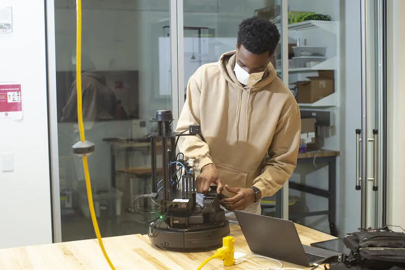 Second-year student Emeka Ezike adjusts his robot during a "CS286: Multi-Robot Systems – Control, Communication, and Security" mini-hack in the Science and Engineering Complex.