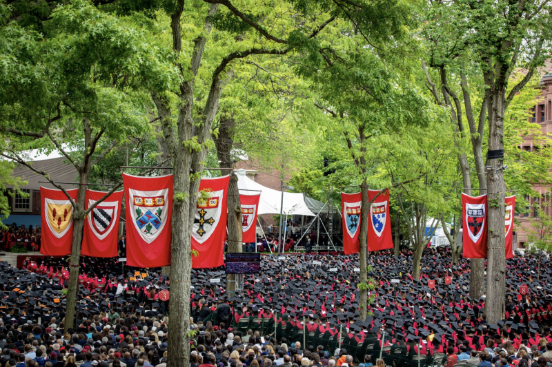 Students sitting in Harvard Yard for Class Day/Commencement with large Harvard banners