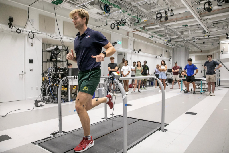 A man running on a treadmill with wires attached to his legs. 