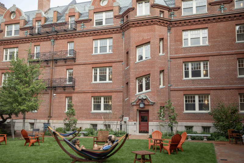 Image of a brick building with windows known as Randolph Hall, with two people sitting in a Hammock outside on a green lawn. 