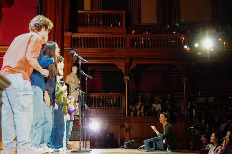 Performers on stage with microphones, while an audience watches.