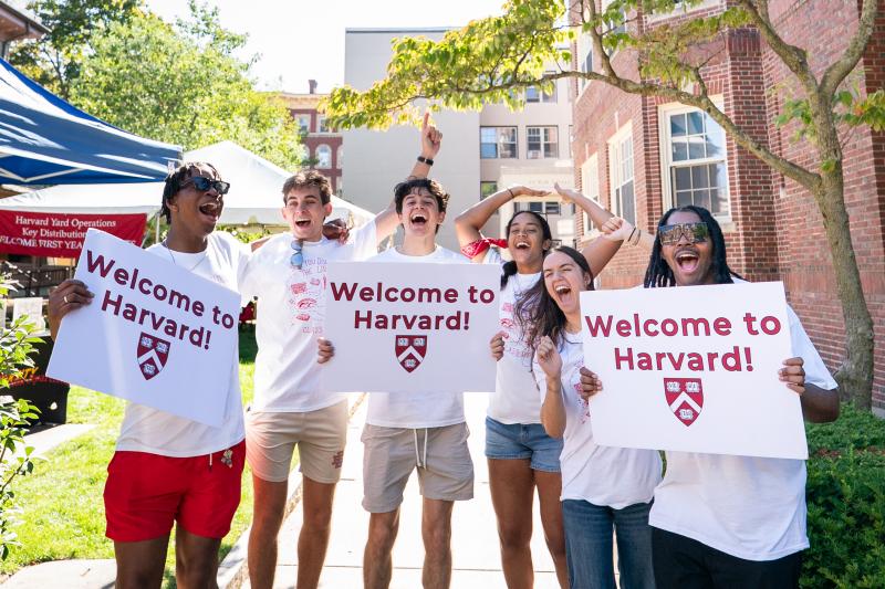 Harvard College students smile while holding "Welcome to Harvard" signs to welcome the incoming class on move-in day.