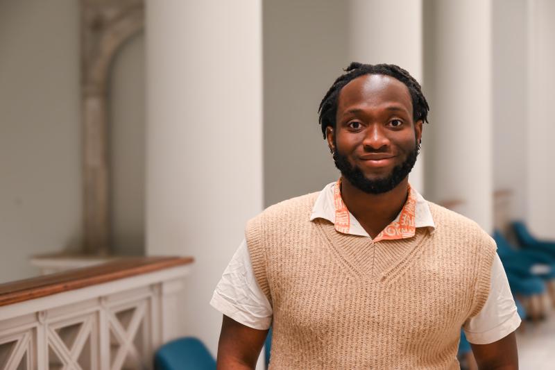 Hassan smiles while standing in a classroom hallway.