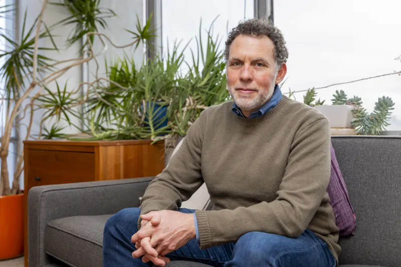 Joshua D. Greene sitting on a couch and staring intently at the camera.