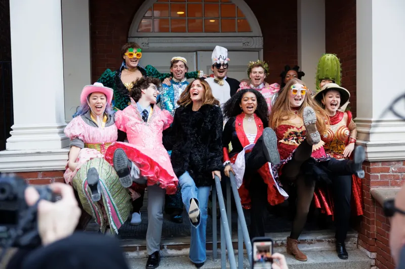 Group of people in colorful costumes laughing and kicking up their legs on steps.