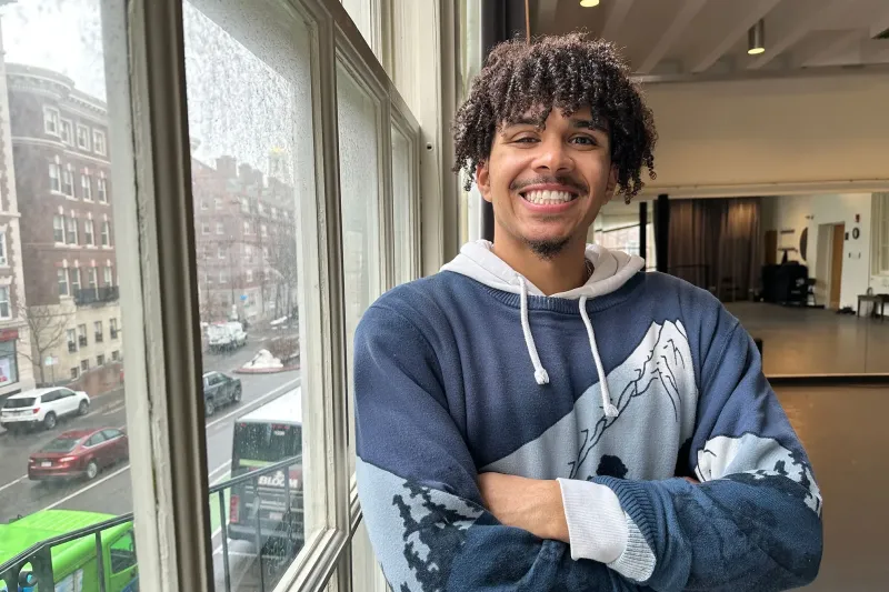 Dree Palimore '25 standing in the Office of the Arts' Director Studio, smiling with his arms crossed next to a window overlooking the street.