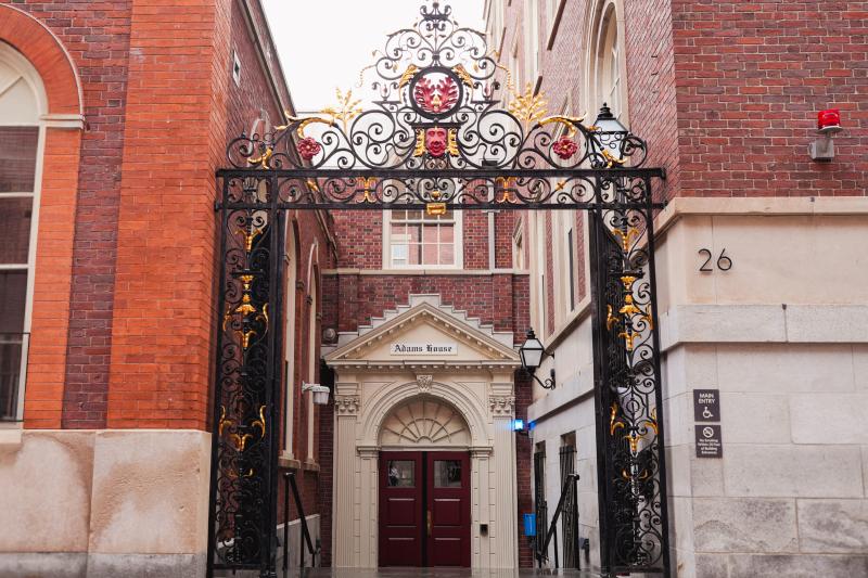  Ornate black and gold wrought-iron gate frames the red double-door entrance to Adams House.