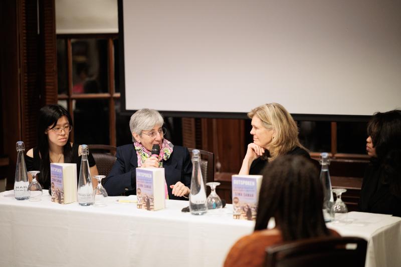 Panel of four women seated at a table with microphones and books, engaged in a discussion.