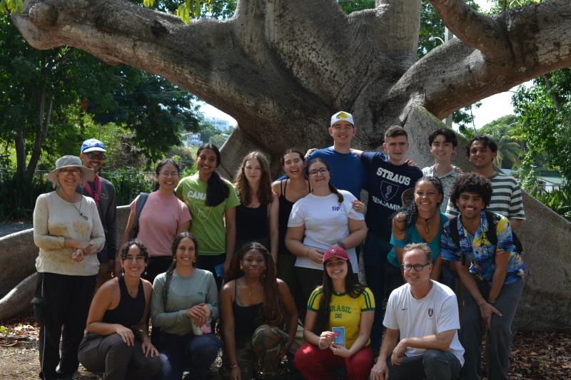 The group of students and two leaders posing together outside next to a large tree.