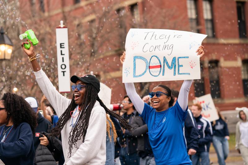 Students holding up a sign for Eliot House that reads "they're coming dome".