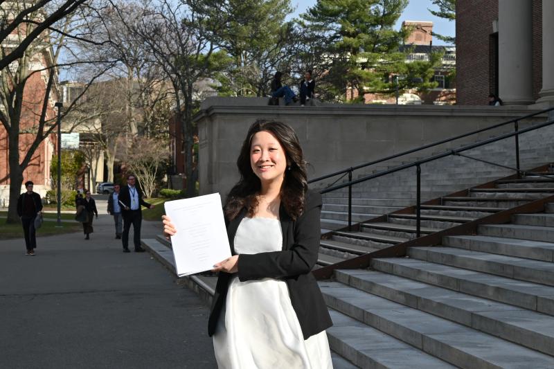Lani Tran '26 standing on the steps of Widener library holding her thesis pages.