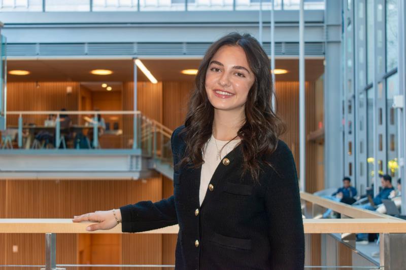 Maria Conforti '28 smiling with an arm on the handrail while inside a Harvard building.