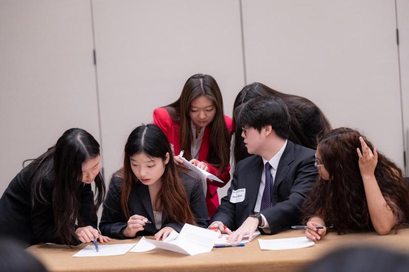 A group of students crowded around a desk and looking through papers.