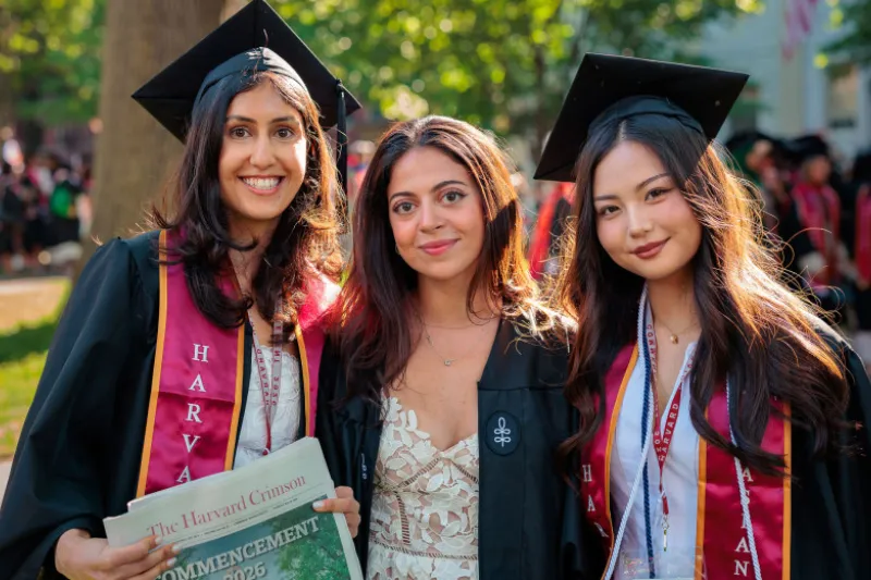Three female students graduating in the Harvard College Class of 2026 smile together on Commencement Day.