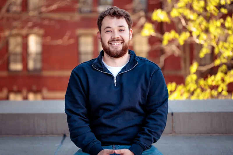 Closeup of Richard Glazunov ’26 with a backdrop of Harvard behind him.