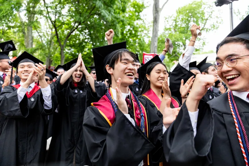 Students cheering in the crowd while wearing their regalia at Commencement.