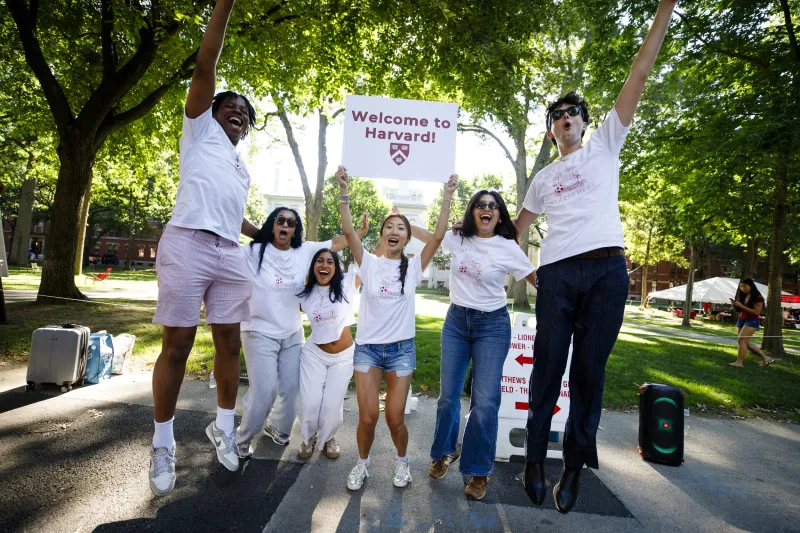 Five students jumping up in the air and cheering while holding a "welcome to harvard" sign.