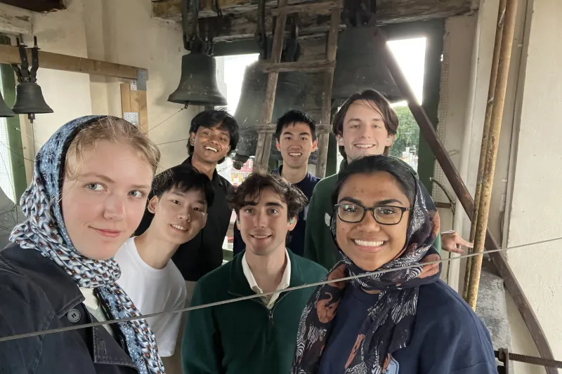 Seven members of the Lowell Bellringers huddled in for a picture together at the top of a belltower in Europe.