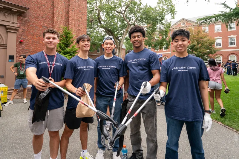 A group of 5 male students holding items to pick up trash.