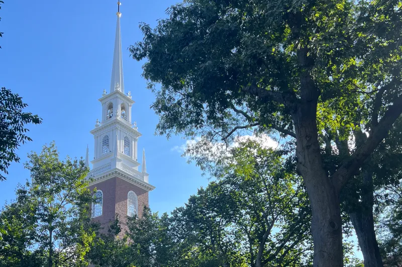 White steeple and brick exterior of Memorial Church framed by lush green trees.