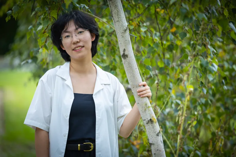 Luna Yin '28 standing outdoors holding onto tree bark and smiling.