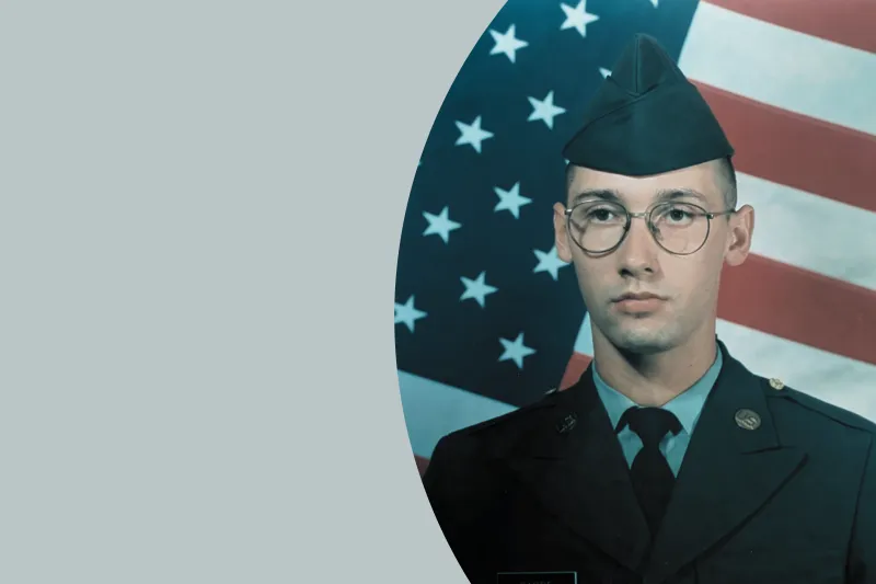 Cory Garbe in his military uniform against a gray background and backdrop of the American flag.