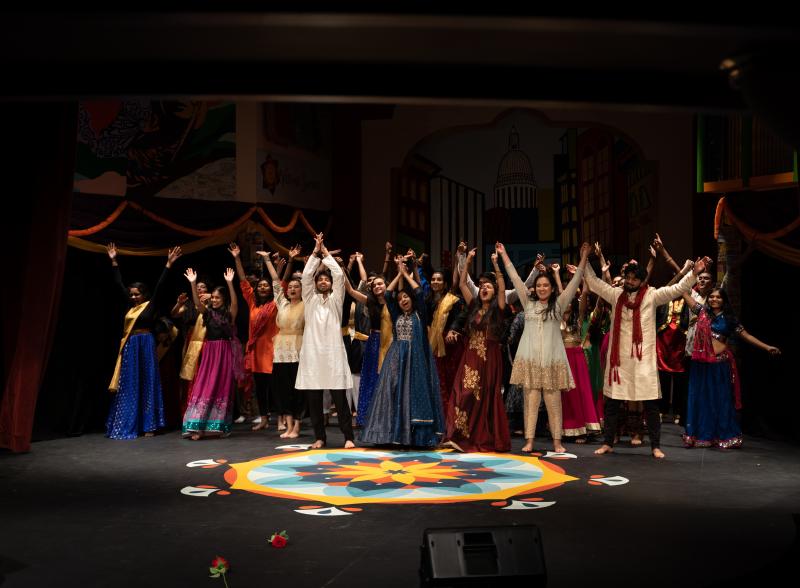 Students wearing South Asian clothing all preparing to bow on stage in the finale of Harvard Ghungroo 2020, with a Rangoli set in front of them.
