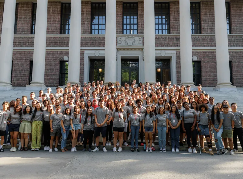 A large group of students gather in front of a library to pose for a picture. 