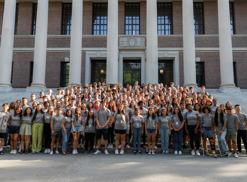 A large group of students gather in front of a library to pose for a picture. 