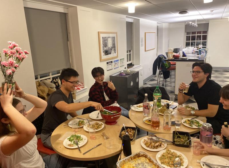 A group of friends sitting around dinner tables, some posing for the picture and some being extra silly for the picture. 