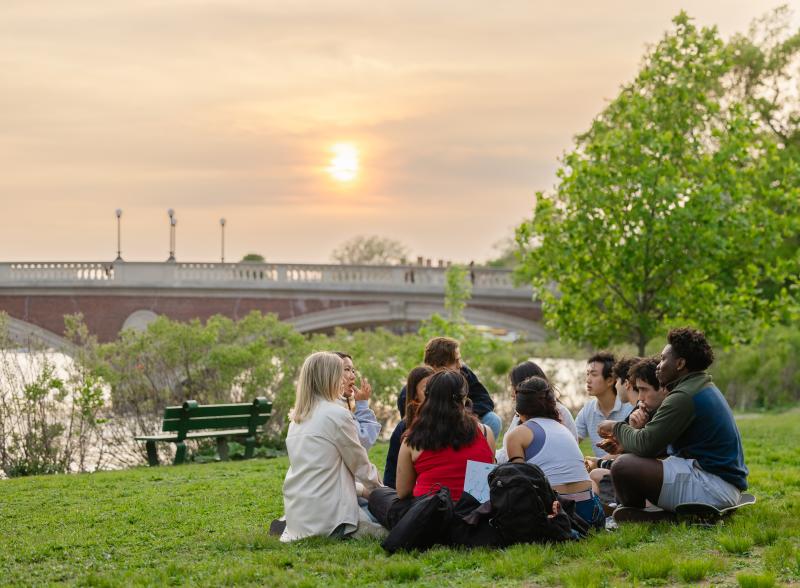 A group of several students sitting on the bank of the Charles River.