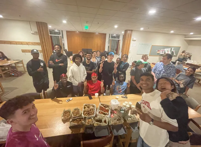Studens gathered around a table full of food 
